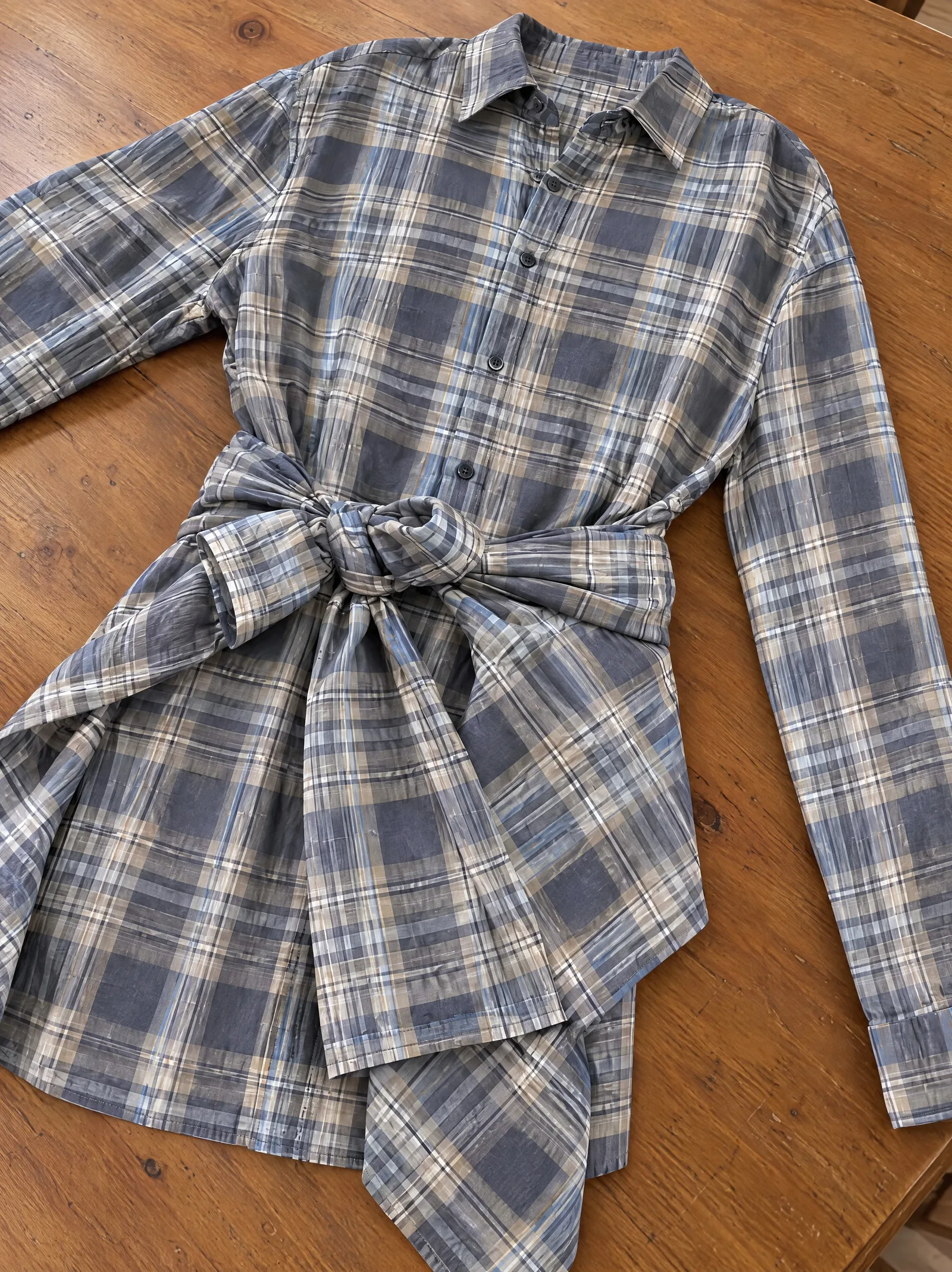 The same shirt dress on a table shot from above at a steep angle, foreshortened, with one sleeve running out of the frame